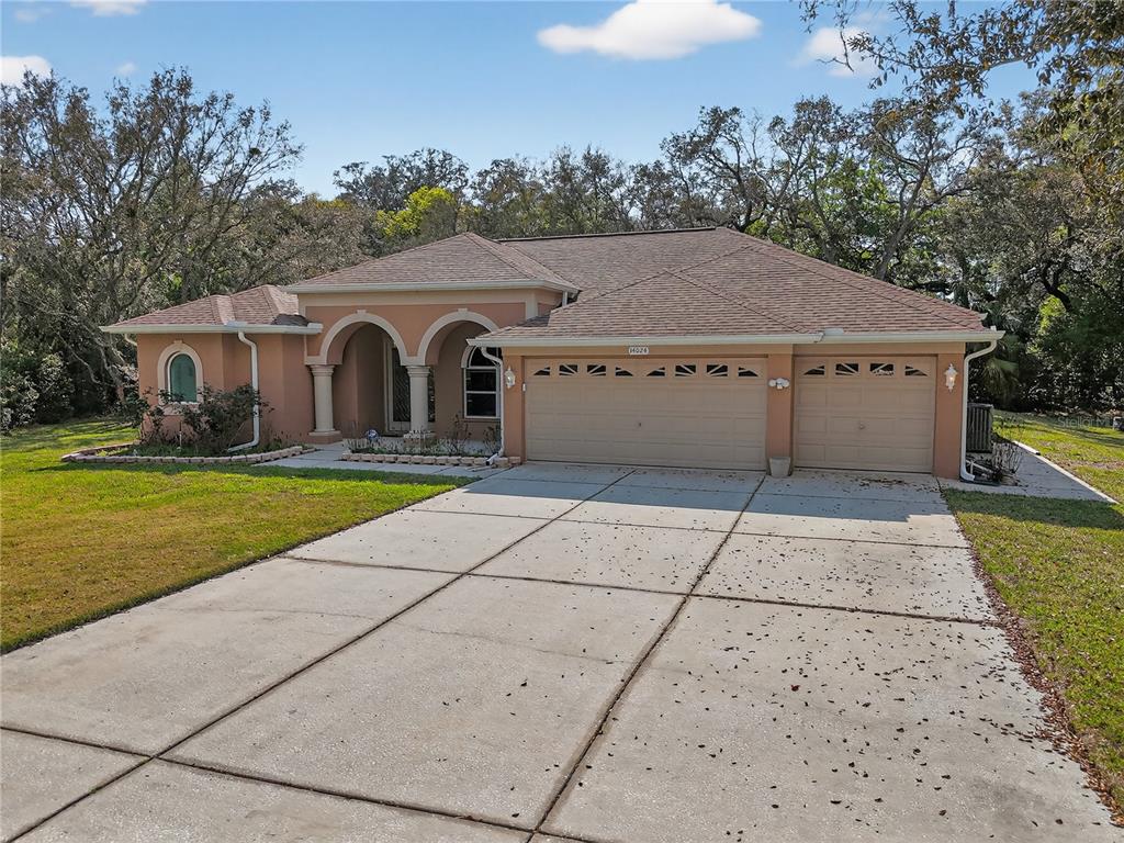 A single-story house with a tan stucco exterior, arched entryway, and a three-car garage — 14024 WARM SPRINGS COURT, HUDSON, FL