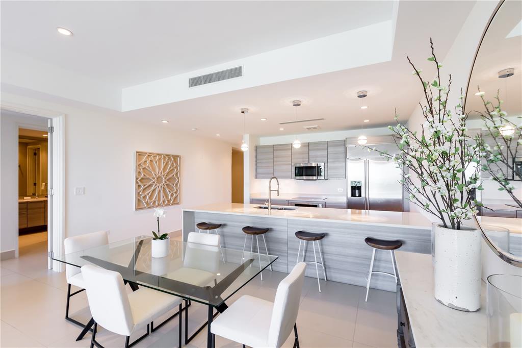 A modern kitchen with a breakfast bar and dining area featuring white chairs and glass table — Bahia Beach Golf Club LAS VENTANAS II UNIT 208, RIO GRANDE, PR
