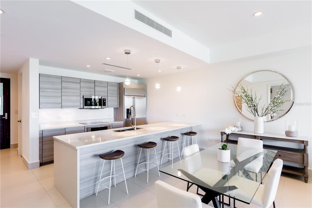 A modern kitchen features light wood cabinetry, a white quartz island with barstools, and dining area — Bahia Beach Golf Club LAS VENTANAS II UNIT 208, RIO GRANDE, PR