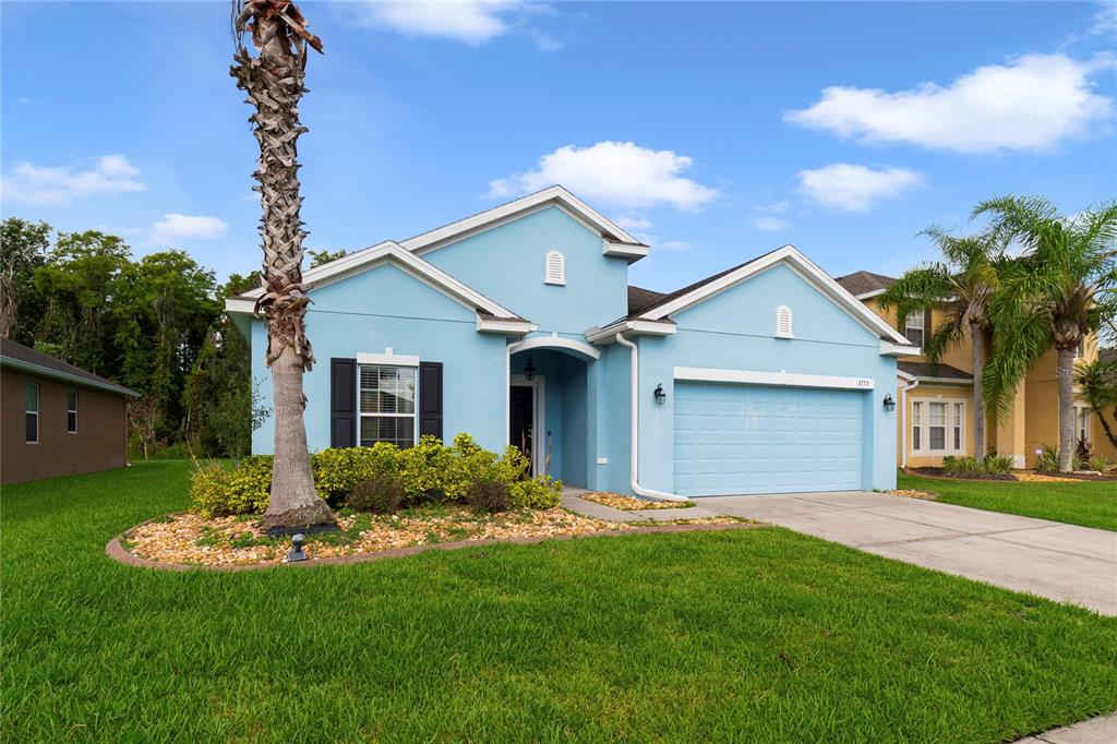 A light blue single-story house with a two-car garage and a palm tree in front — 3773 MOON DANCER PLACE, ST CLOUD, FL