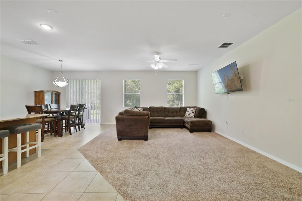A living room and dining area with tile floors, carpet, and a mounted television — 3773 MOON DANCER PLACE, ST CLOUD, FL