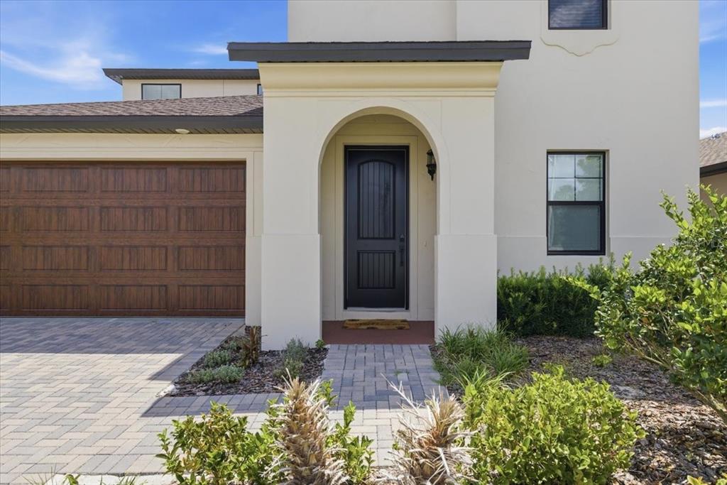 A beige house exterior features a dark front door, arched entryway, and a brown garage — 82 HILLSHIRE PLACE, SPRING HILL, FL