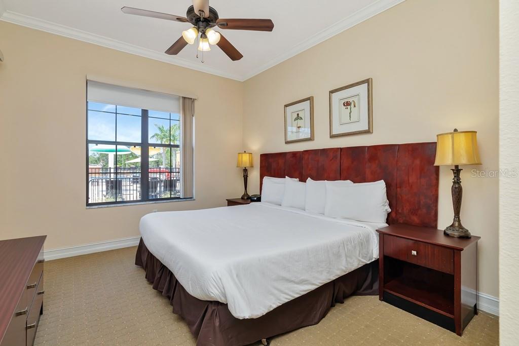 A bedroom features a king bed, a dark wood headboard, and a view of a pool — 13941 CLUBHOUSE DRIVE UNIT 103, TAMPA, FL