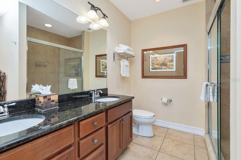A bathroom features a double vanity with granite countertops, a toilet, and a glass shower — 13941 CLUBHOUSE DRIVE UNIT 103, TAMPA, FL