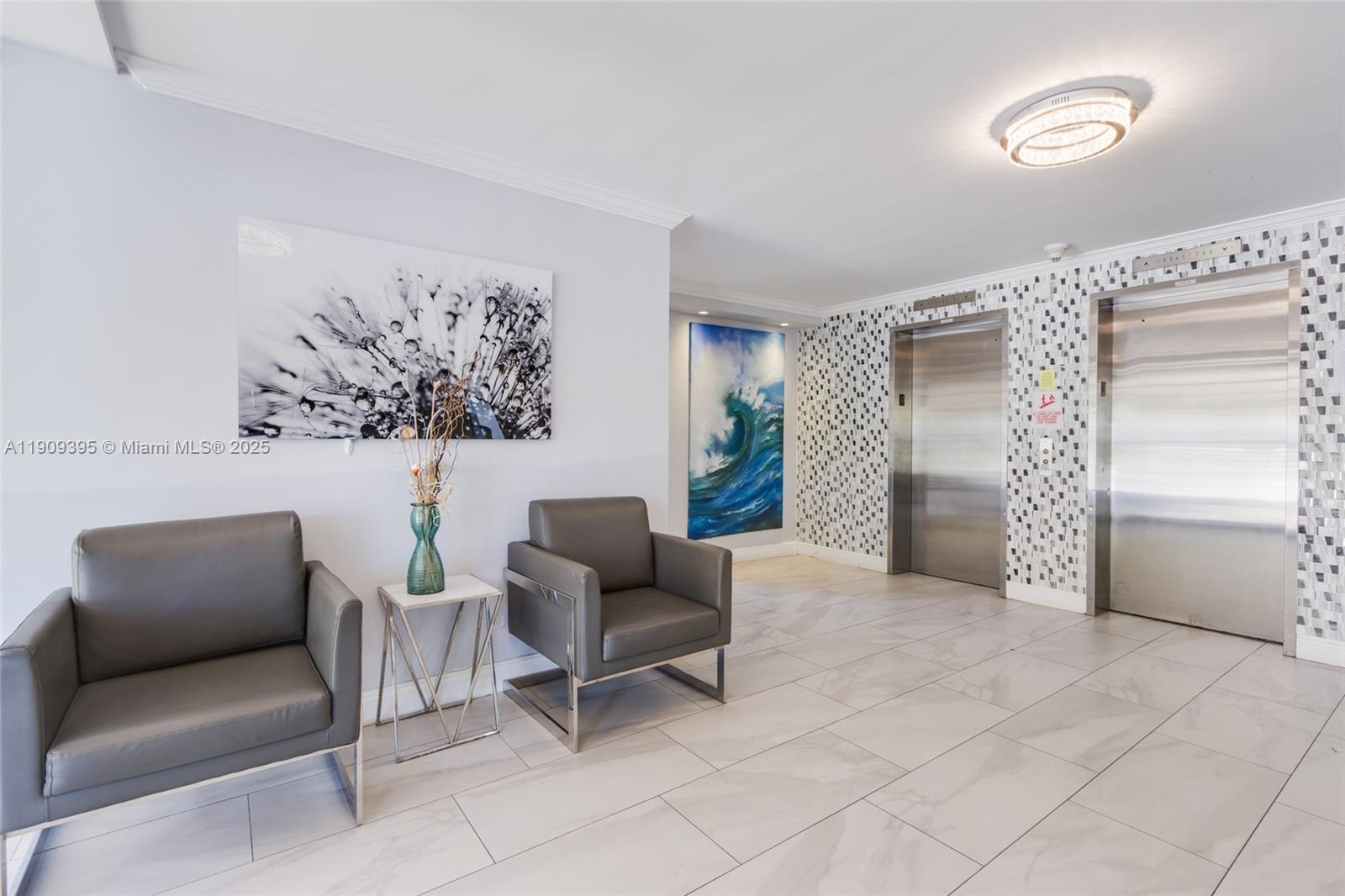A modern building lobby features two gray armchairs, a side table, and two stainless elevators — 2671 S Course Dr # 506, Pompano Beach FL 33069, POMPANO BEACH, FL