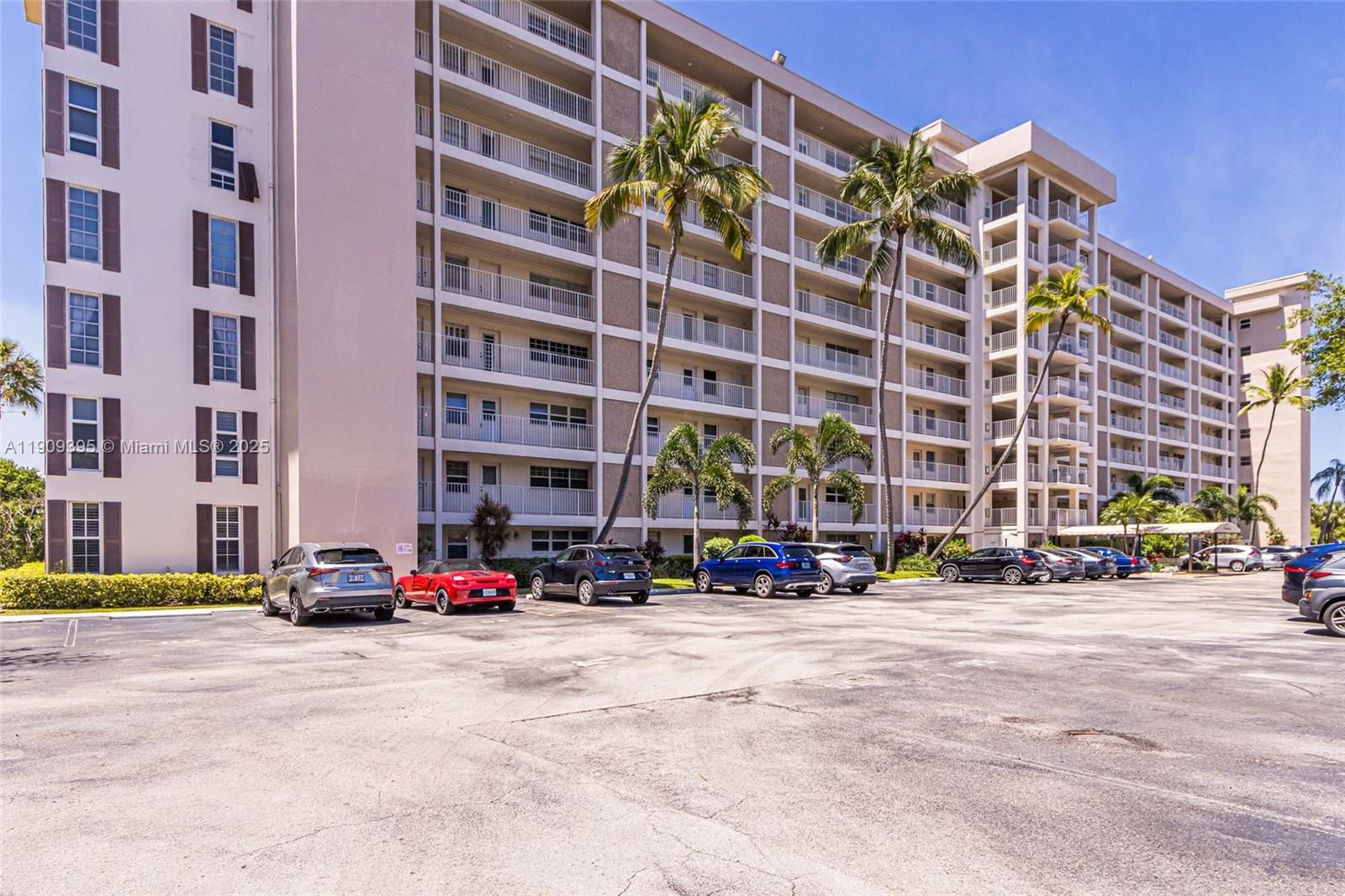 A multi-story apartment building features balconies and a parking lot with several parked cars — 2671 S Course Dr # 506, Pompano Beach FL 33069, POMPANO BEACH, FL