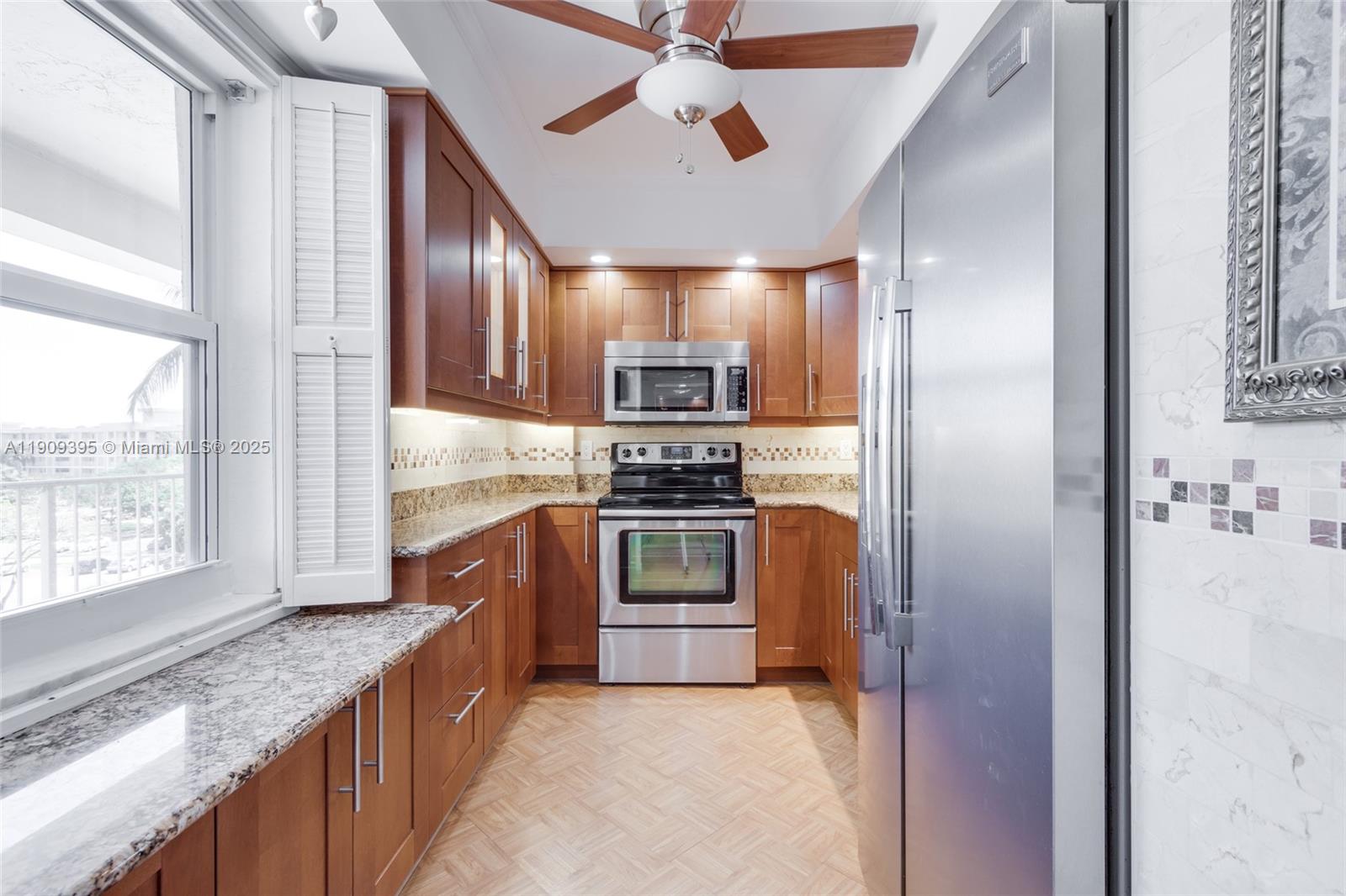 A galley kitchen features wood cabinets, stainless steel appliances, granite countertops, and a ceiling fan — 2671 S Course Dr # 506, Pompano Beach FL 33069, POMPANO BEACH, FL