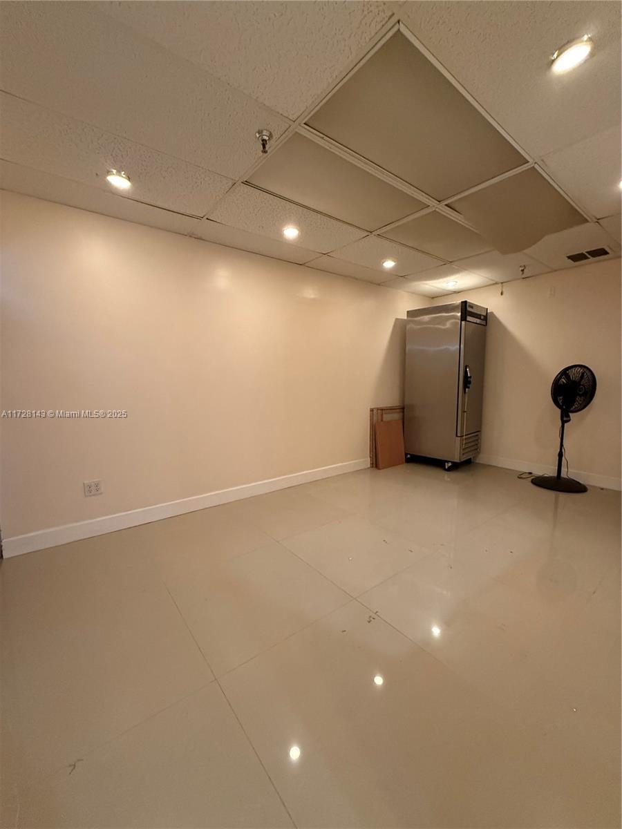 An empty room features a drop ceiling, recessed lighting, a stainless steel refrigerator, and tile flooring — 777 NW 72nd Ave # 2131, Miami FL 33126, MIAMI, FL