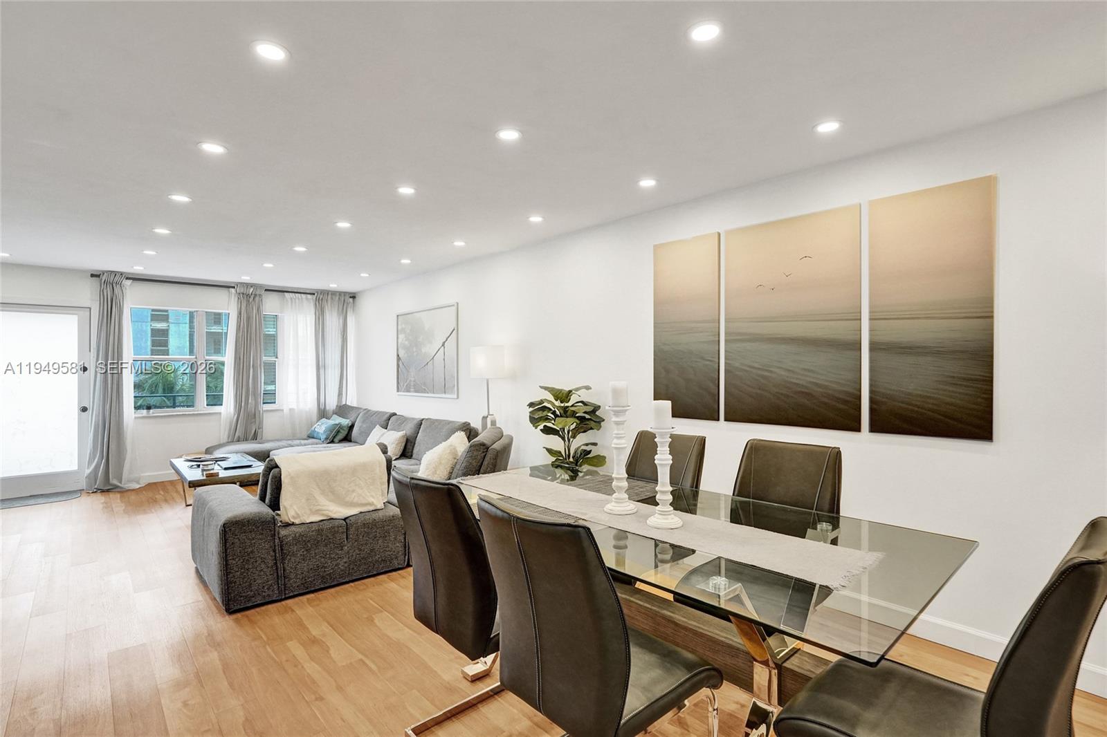A dining area with a glass table and chairs sits adjacent to a living room — 401 Golden Isles Dr # 302, Hallandale Beach FL 33009, HALLANDALE BEACH, FL
