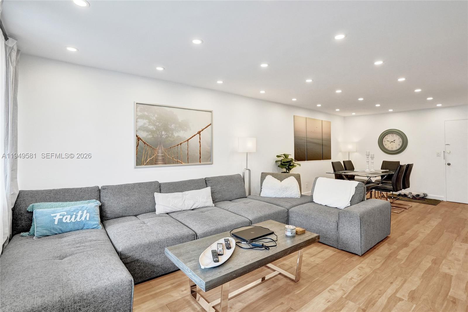 A living room features a large gray sectional sofa, a coffee table, and dining area — 401 Golden Isles Dr # 302, Hallandale Beach FL 33009, HALLANDALE BEACH, FL
