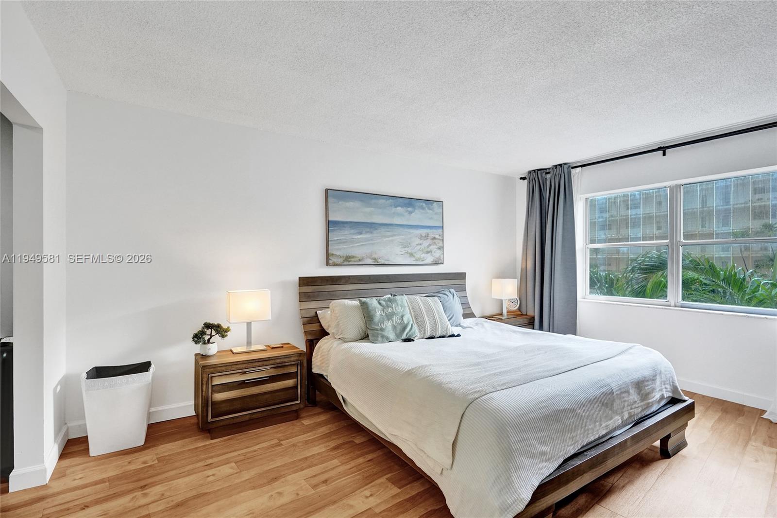A bedroom features a wooden bed frame, two nightstands, and a window with gray curtains — 401 Golden Isles Dr # 302, Hallandale Beach FL 33009, HALLANDALE BEACH, FL