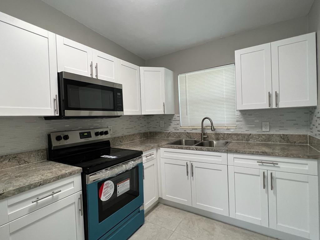 A kitchen features white cabinets, stainless steel appliances, a tiled backsplash, and stone-look countertops — 3990 Plum Tree Drive, Lake Worth FL 33462, LAKE WORTH, FL