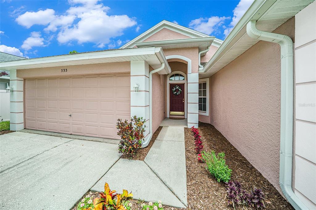 A pink stucco house exterior features a two-car garage, a front entryway, and landscaped beds — 333 TAVERNIER DRIVE, OLDSMAR, FL