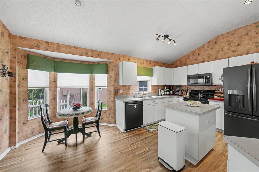 A kitchen features white cabinets, black appliances, a small island, and floral wallpaper — 333 TAVERNIER DRIVE, OLDSMAR, FL