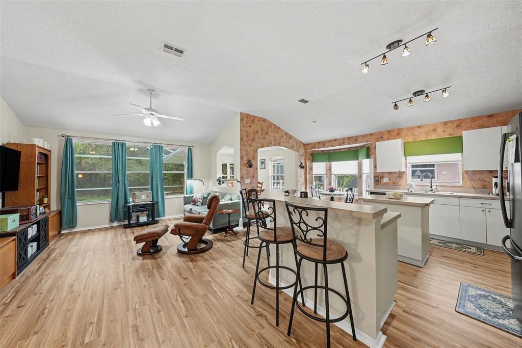 An open-concept living room and kitchen featuring wood-look flooring, vaulted ceilings, and a breakfast bar — 333 TAVERNIER DRIVE, OLDSMAR, FL