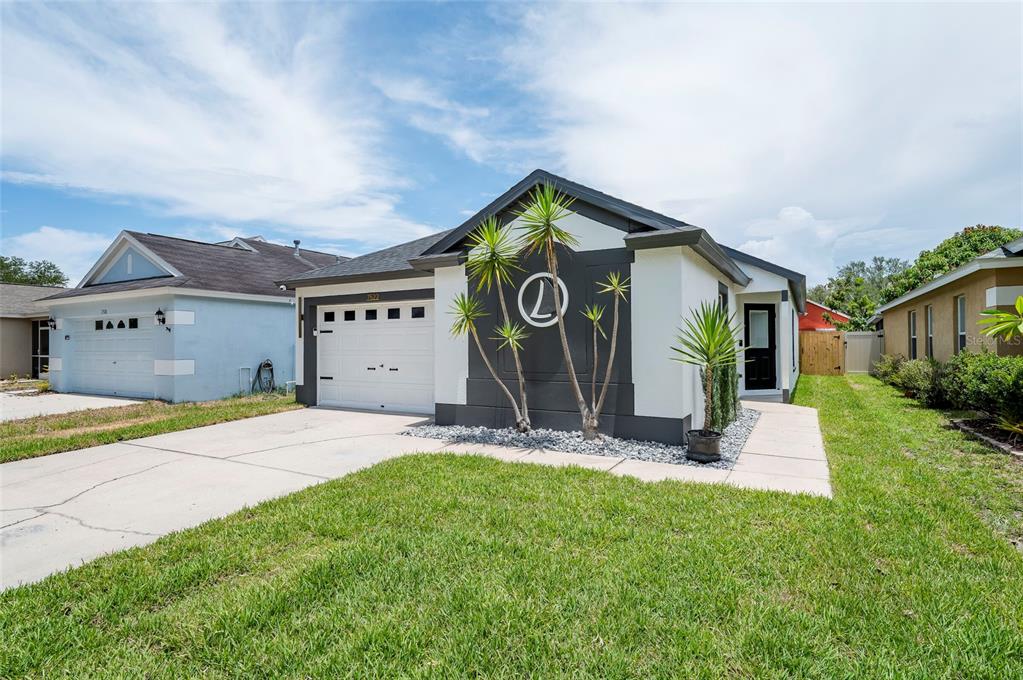 A single-story house with a white and dark gray exterior, a garage, and palm trees — 7522 OXFORD GARDEN CIRCLE, APOLLO BEACH, FL