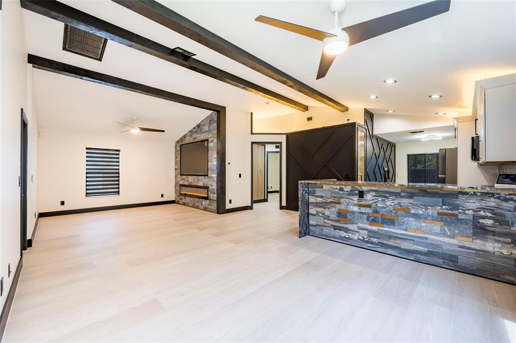 An open-concept living area features light wood floors, exposed ceiling beams, and stone accents — 7522 OXFORD GARDEN CIRCLE, APOLLO BEACH, FL