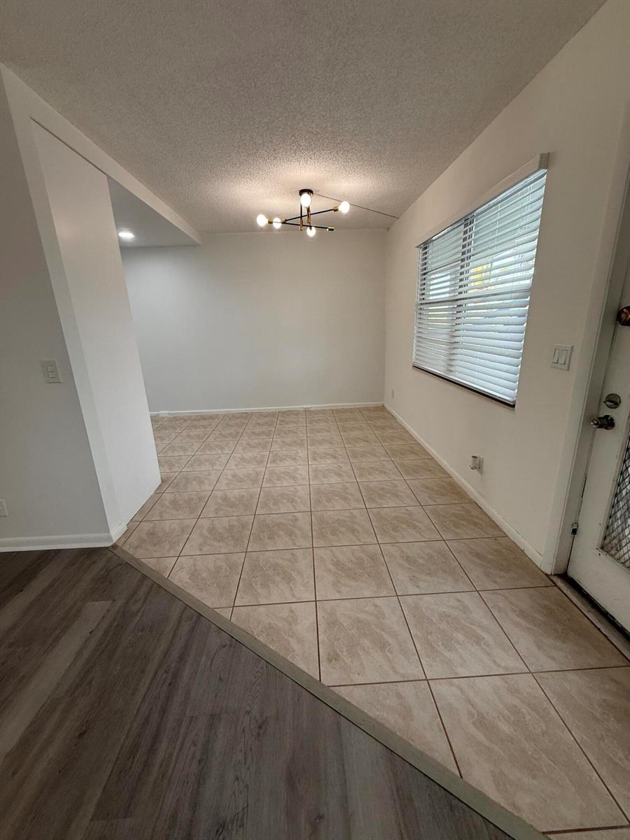 An empty dining area features beige tile flooring, a modern chandelier, and a window with blinds — 3089 Yarmouth E # 3089, Boca Raton FL 33434, BOCA RATON, FL