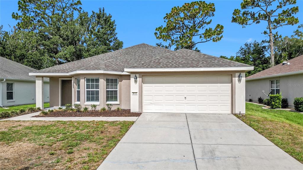 A single-story house with a beige stucco exterior, a two-car garage, and a concrete driveway — 9119 SE 120TH LOOP, SUMMERFIELD, FL