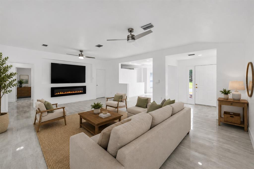A bright living room features a fireplace, a large television, and light-colored tile flooring — 9119 SE 120TH LOOP, SUMMERFIELD, FL