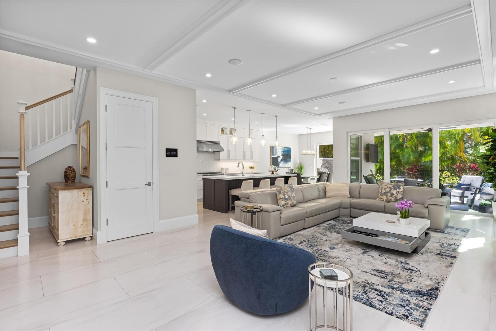An open-concept living room features a large sectional, blue armchair, and a modern kitchen — 444 NE Wavecrest Way, Boca Raton FL 33432, BOCA RATON, FL