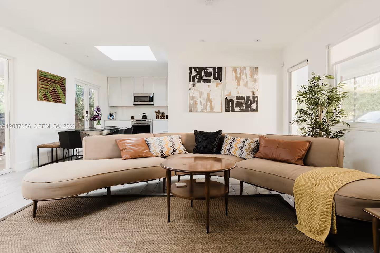 A living room features a curved beige sofa, a round wooden table, and an open kitchen — 424 NE 28th Dr, Wilton Manors FL 33334, WILTON MANORS, FL