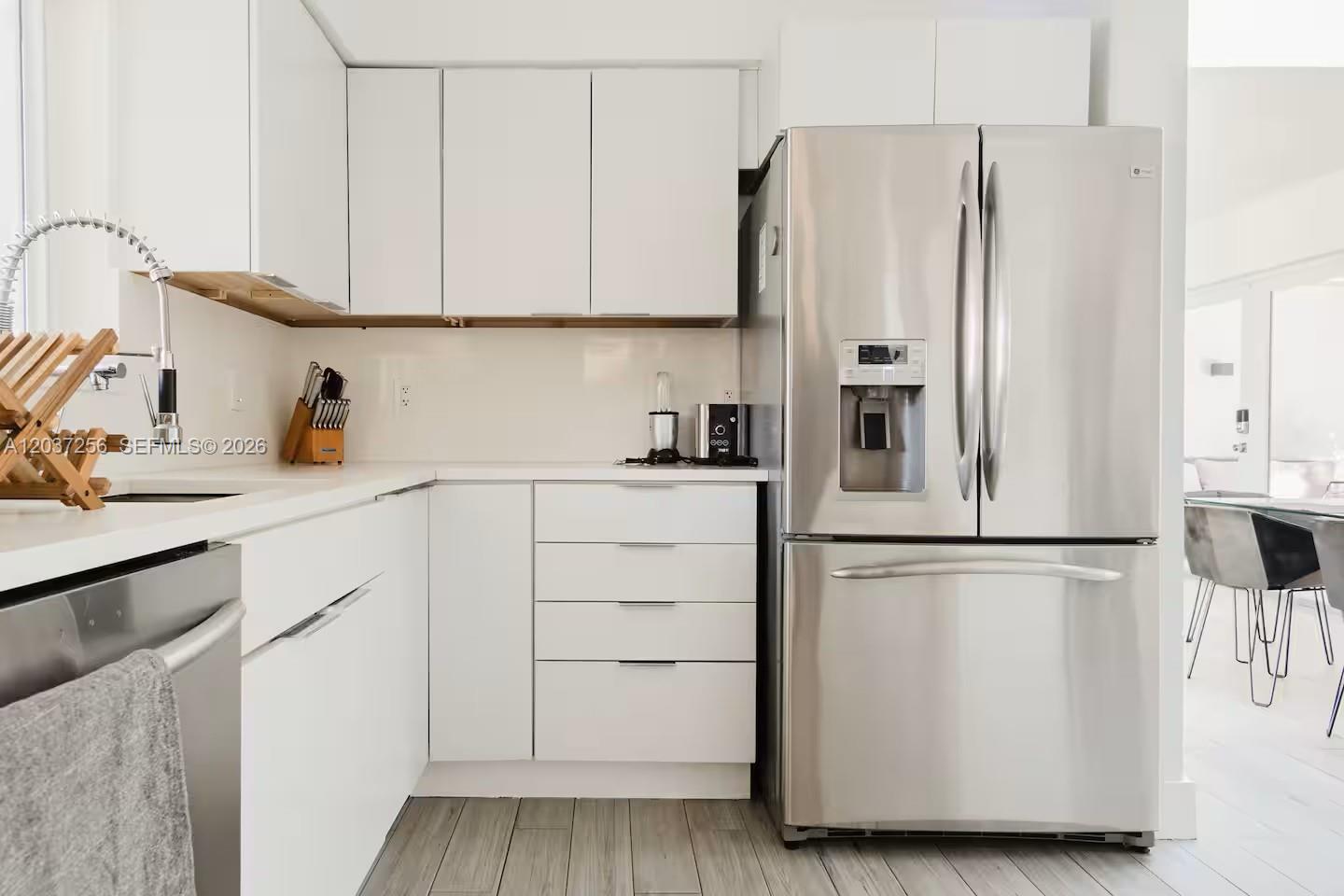 A modern kitchen features white cabinetry, stainless steel appliances, and light wood-look flooring — 424 NE 28th Dr, Wilton Manors FL 33334, WILTON MANORS, FL
