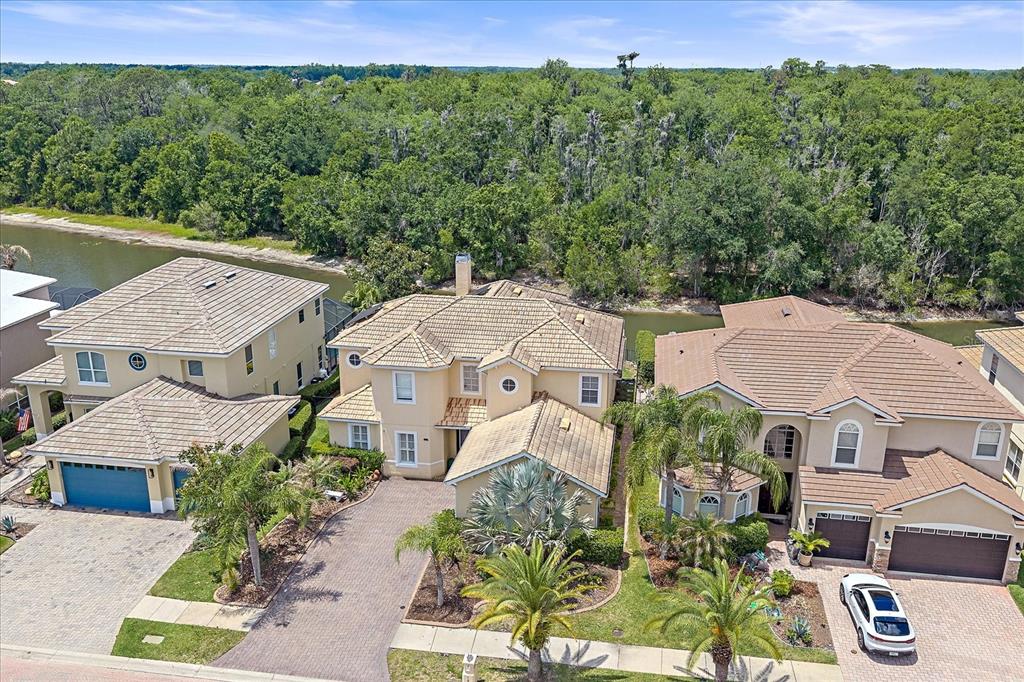 An aerial view shows three suburban houses with tile roofs situated along a narrow waterway — 18046 COZUMEL ISLE DRIVE, TAMPA, FL