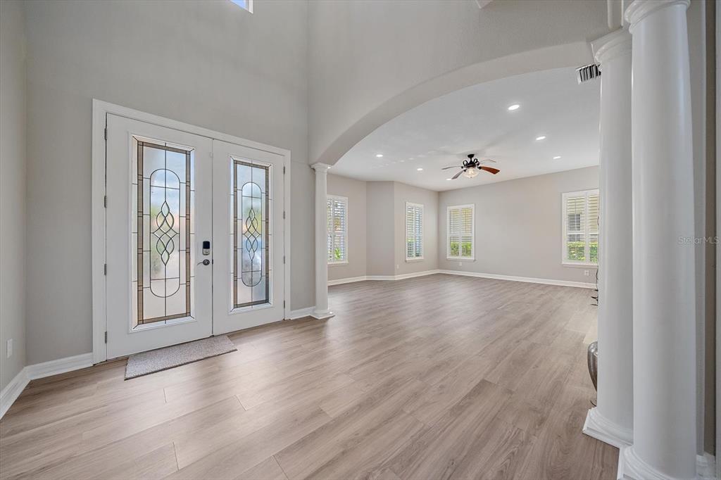 A bright entryway with light wood flooring leads into a spacious room with white columns — 18046 COZUMEL ISLE DRIVE, TAMPA, FL