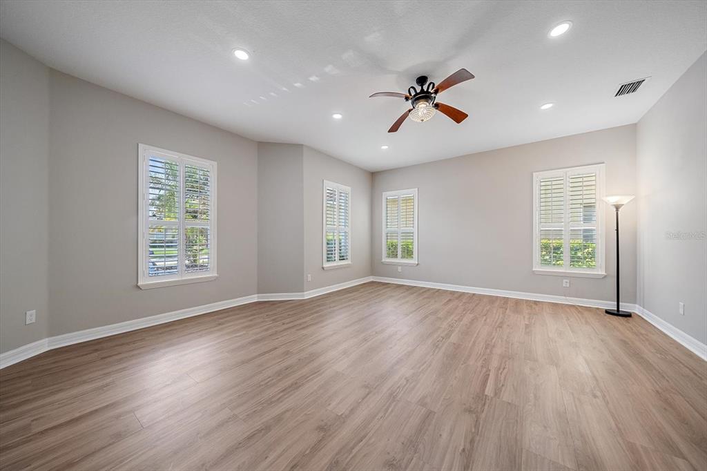 An empty room features light wood-look flooring, gray walls, recessed lighting, and white plantation shutters — 18046 COZUMEL ISLE DRIVE, TAMPA, FL