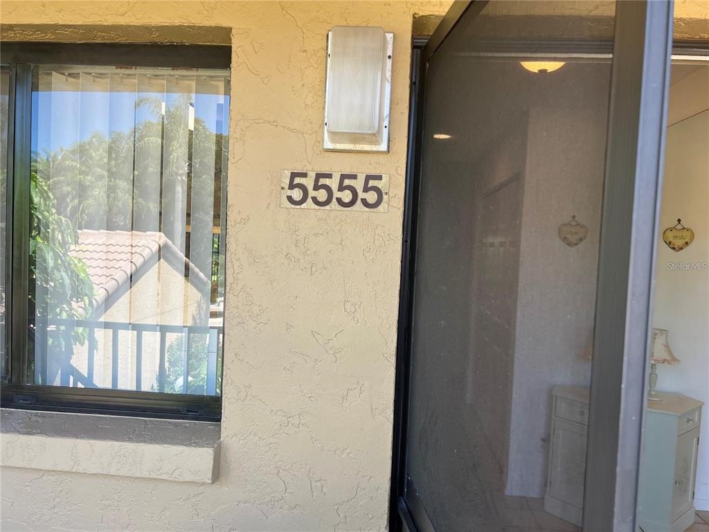 The exterior view shows a building entrance with a house number, a window, and a screen door — 5555 ASHTON WAY UNIT 5555, SARASOTA, FL