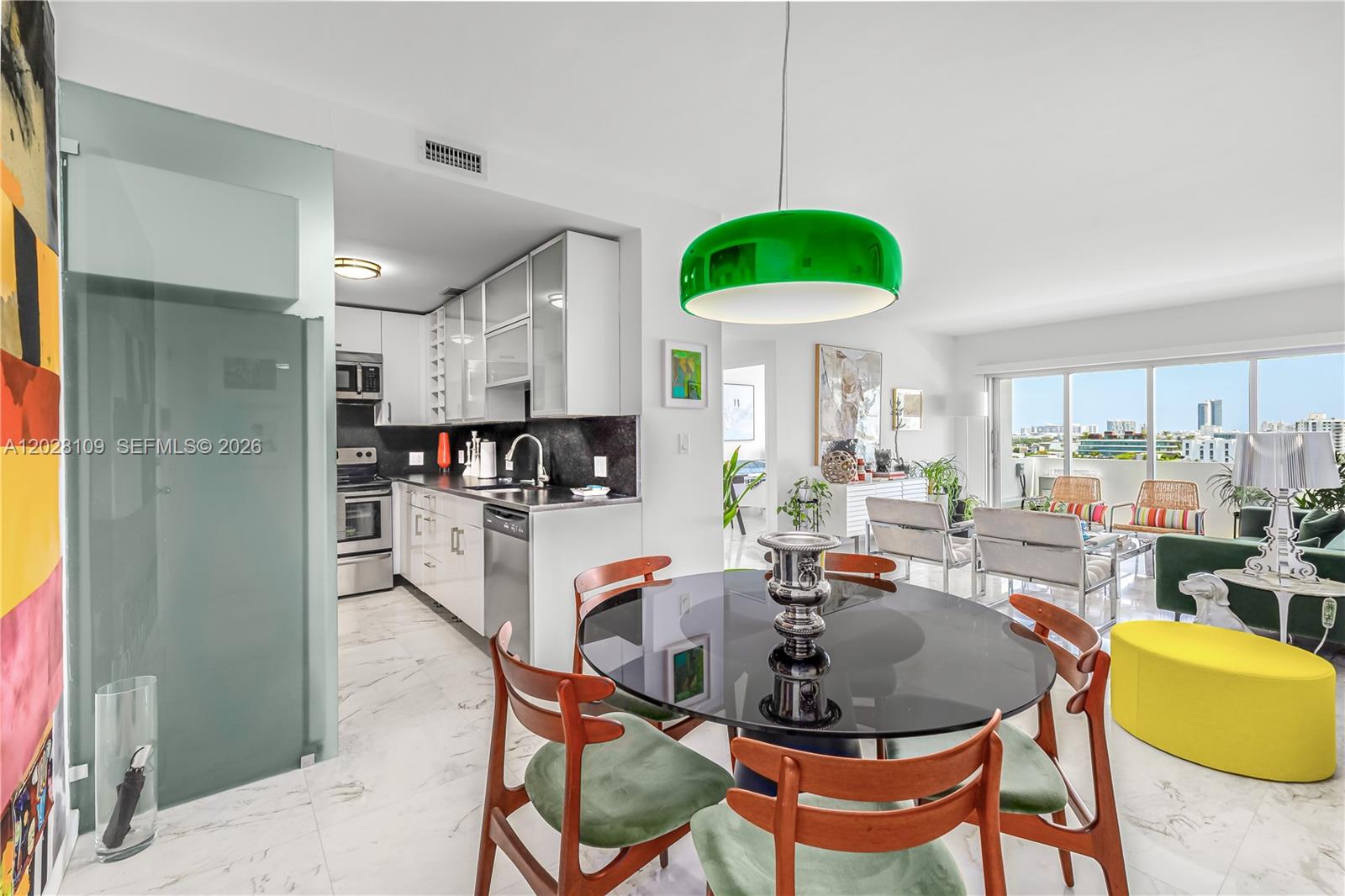 A modern dining area with a glass table and green chairs opens into a kitchen — 3 Island Ave # 11B, Miami Beach FL 33139, MIAMI BEACH, FL