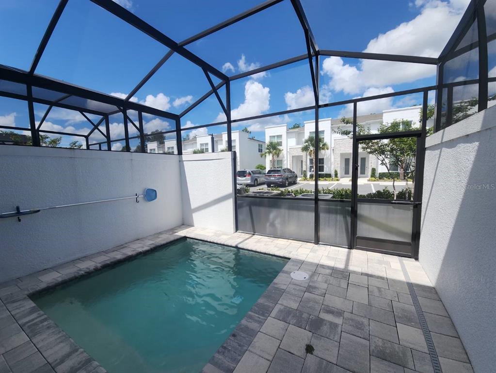 A small rectangular swimming pool is enclosed by a screened lanai with white stucco walls — 1393 PEACEFUL NATURE WAY, CLERMONT, FL