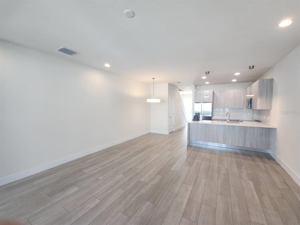 An open-concept kitchen and living area features light wood-look flooring and modern cabinetry — 1393 PEACEFUL NATURE WAY, CLERMONT, FL