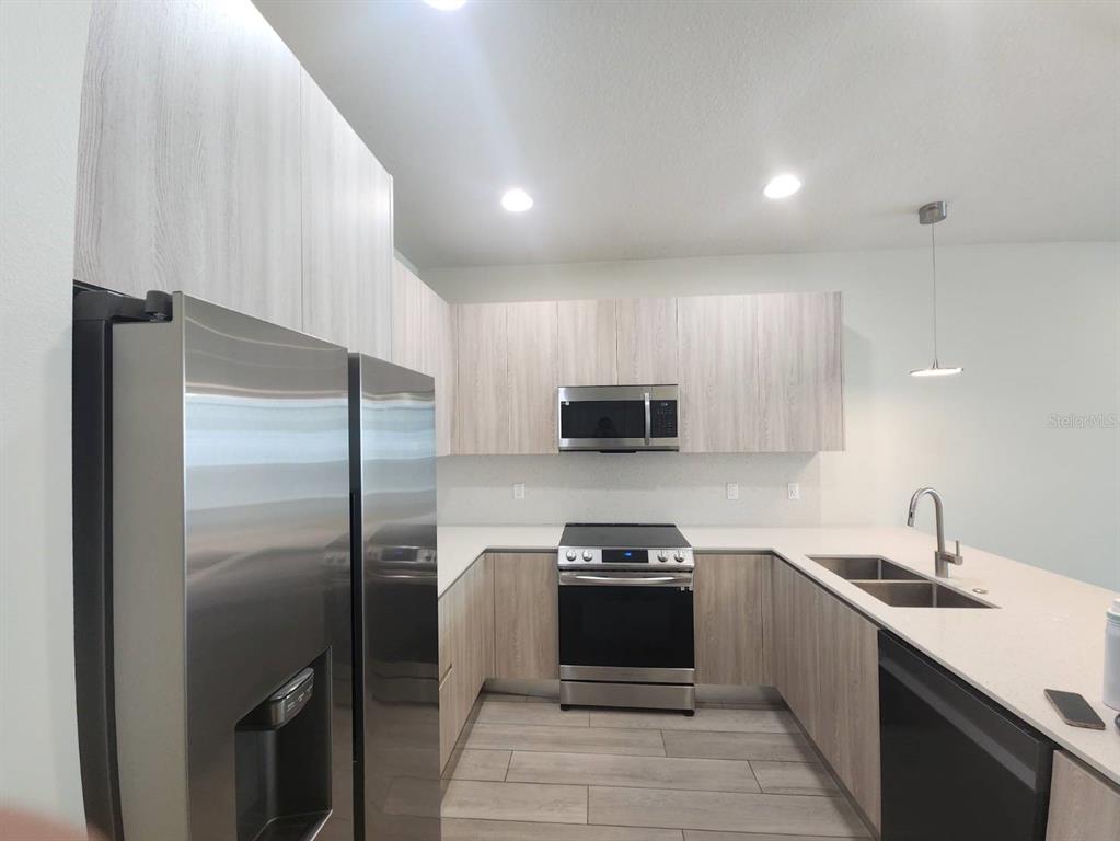 A modern kitchen features light wood cabinets, stainless steel appliances, and a white countertop — 1393 PEACEFUL NATURE WAY, CLERMONT, FL