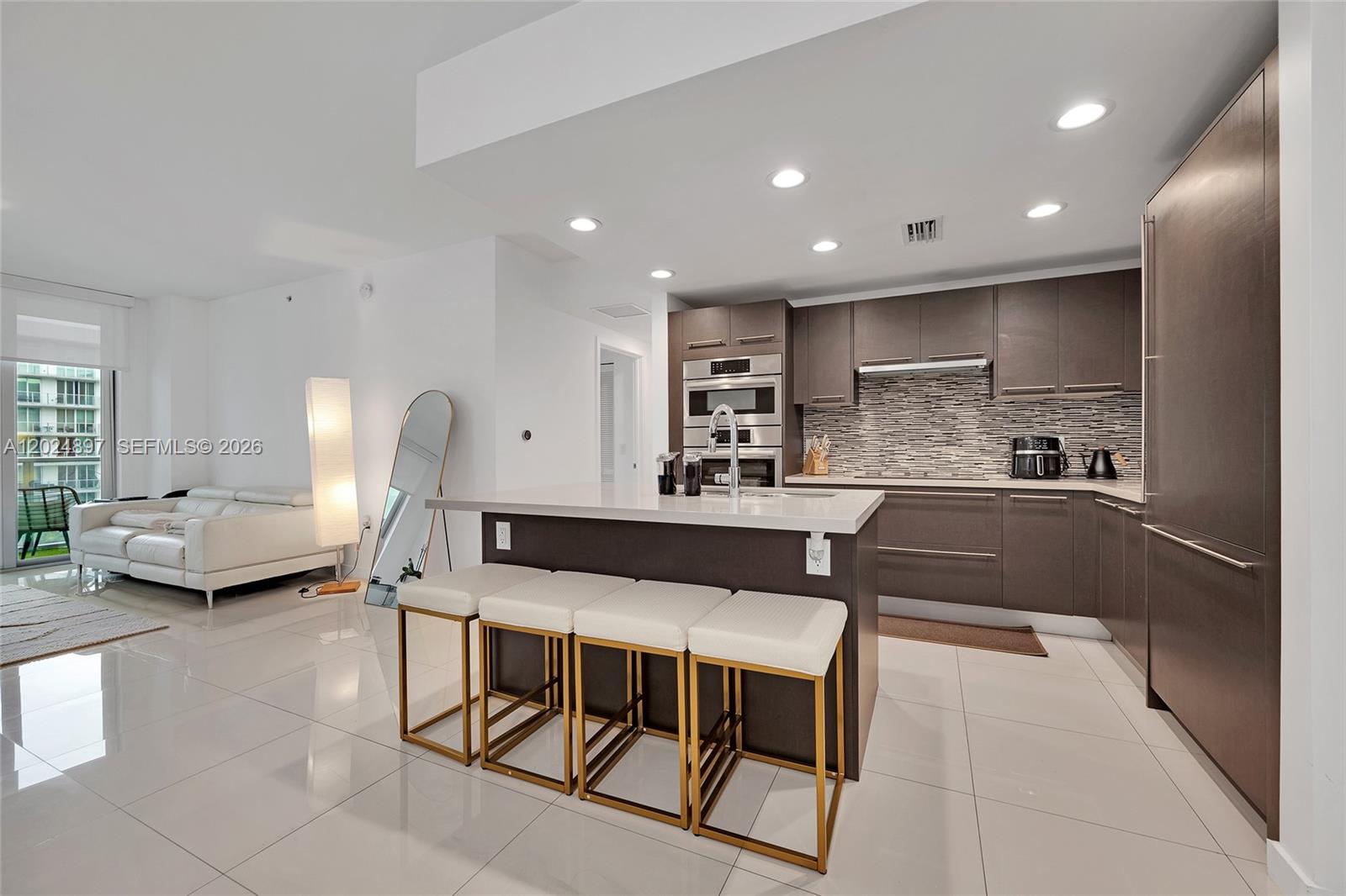 A modern kitchen features dark cabinetry, a white island with four stools, and tile flooring — 7825 NW 107th Ave # 507, Doral FL 33178, DORAL, FL