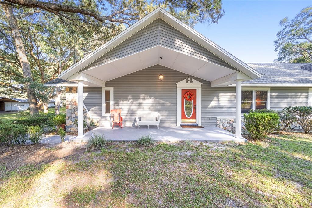 A gray-sided house features a covered front porch with white columns and a red door — 13315 NE 47TH AVENUE, ANTHONY, FL
