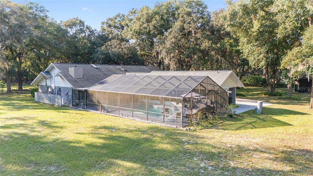 An exterior view of a house with a screened-in pool and a large grassy yard — 13315 NE 47TH AVENUE, ANTHONY, FL