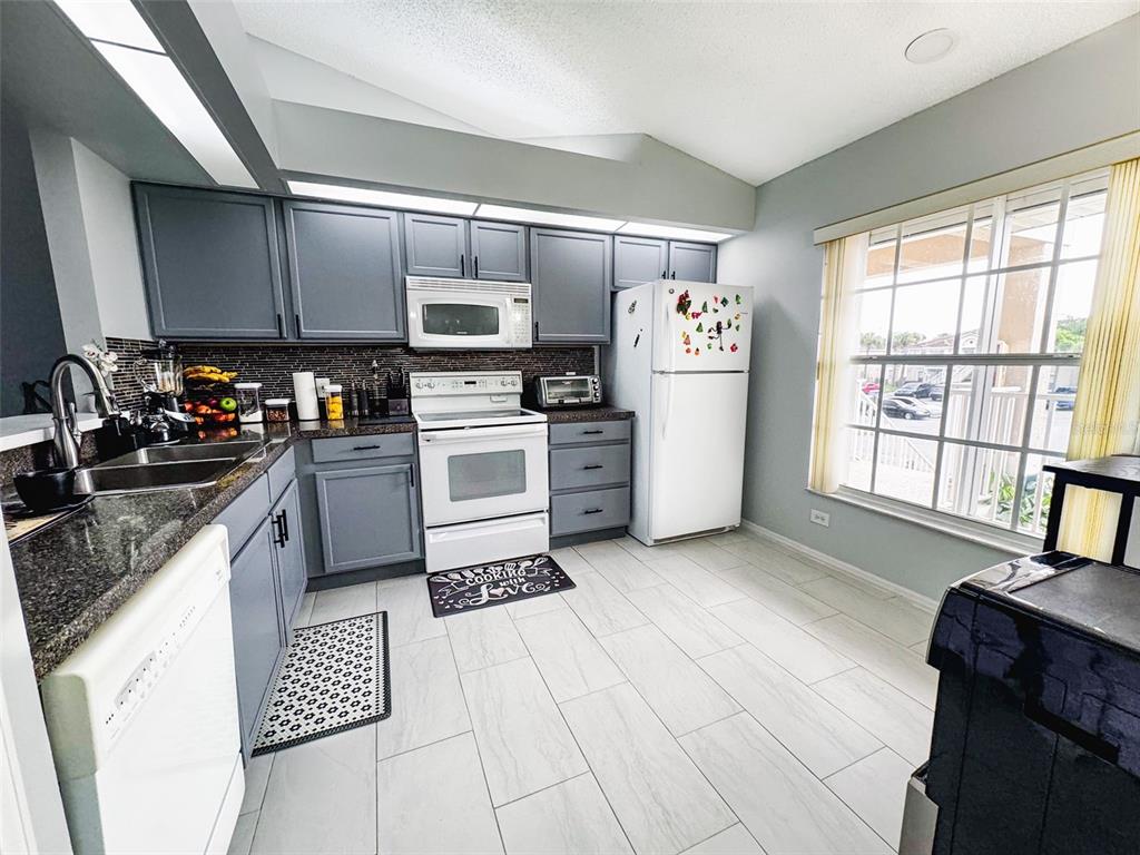 A kitchen features gray cabinets, dark countertops, white appliances, and light-colored tile flooring — 13801 TIMBERLAND DRIVE UNIT 201, ORLANDO, FL