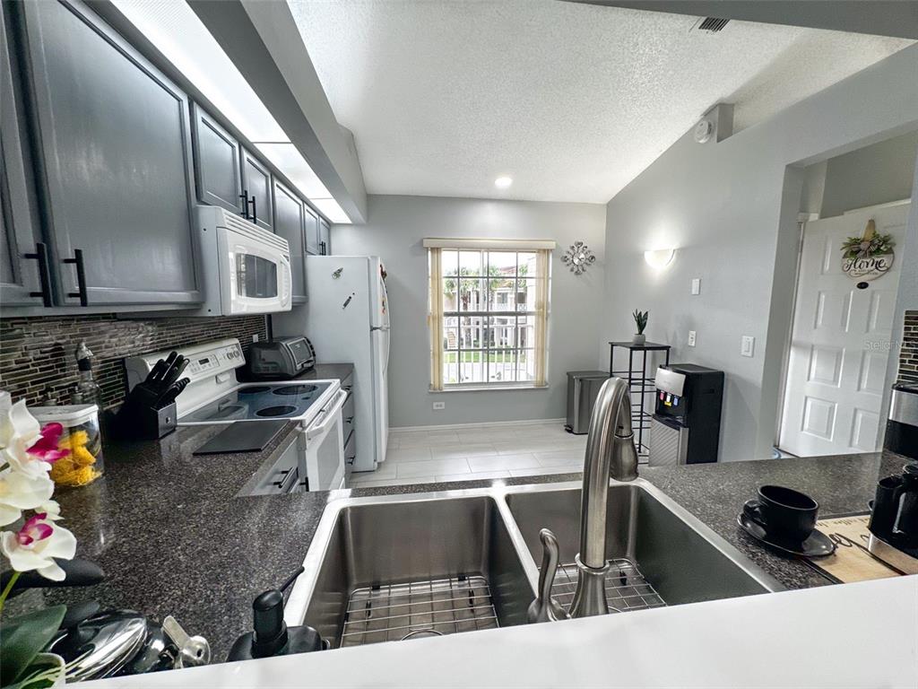 A kitchen features dark gray cabinets, granite countertops, a double sink, and a window view — 13801 TIMBERLAND DRIVE UNIT 201, ORLANDO, FL
