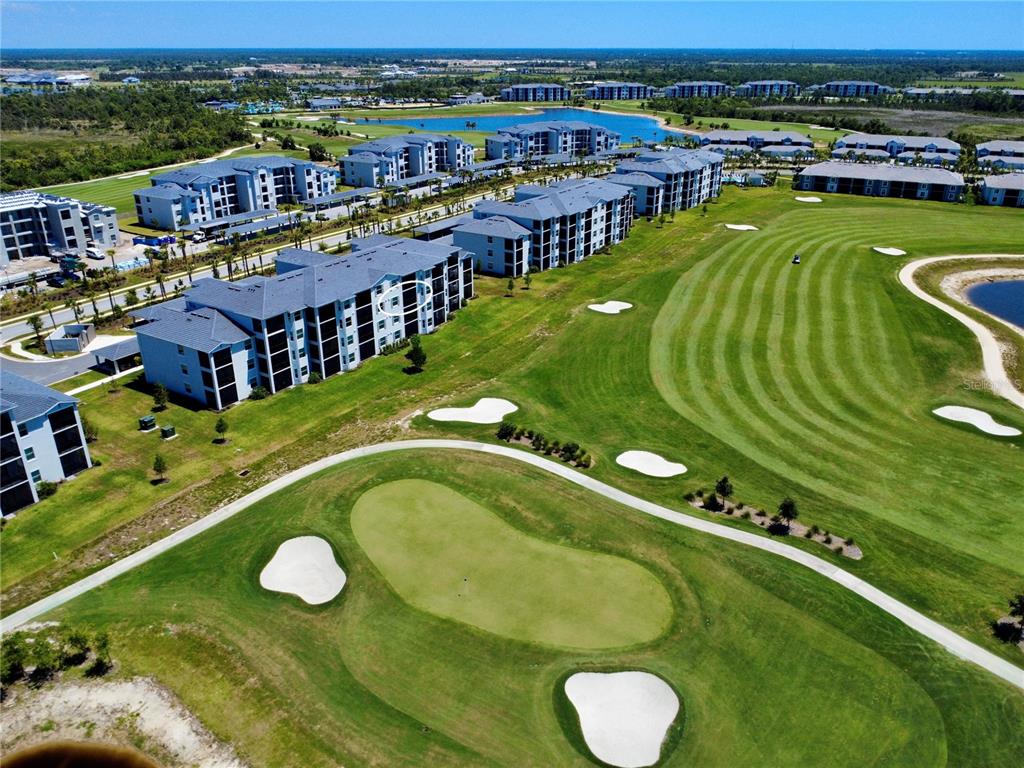 An aerial view shows multi-story apartment buildings situated alongside a golf course with sand bunkers — 17625 OPAL SAND DRIVE UNIT 304, VENICE, FL