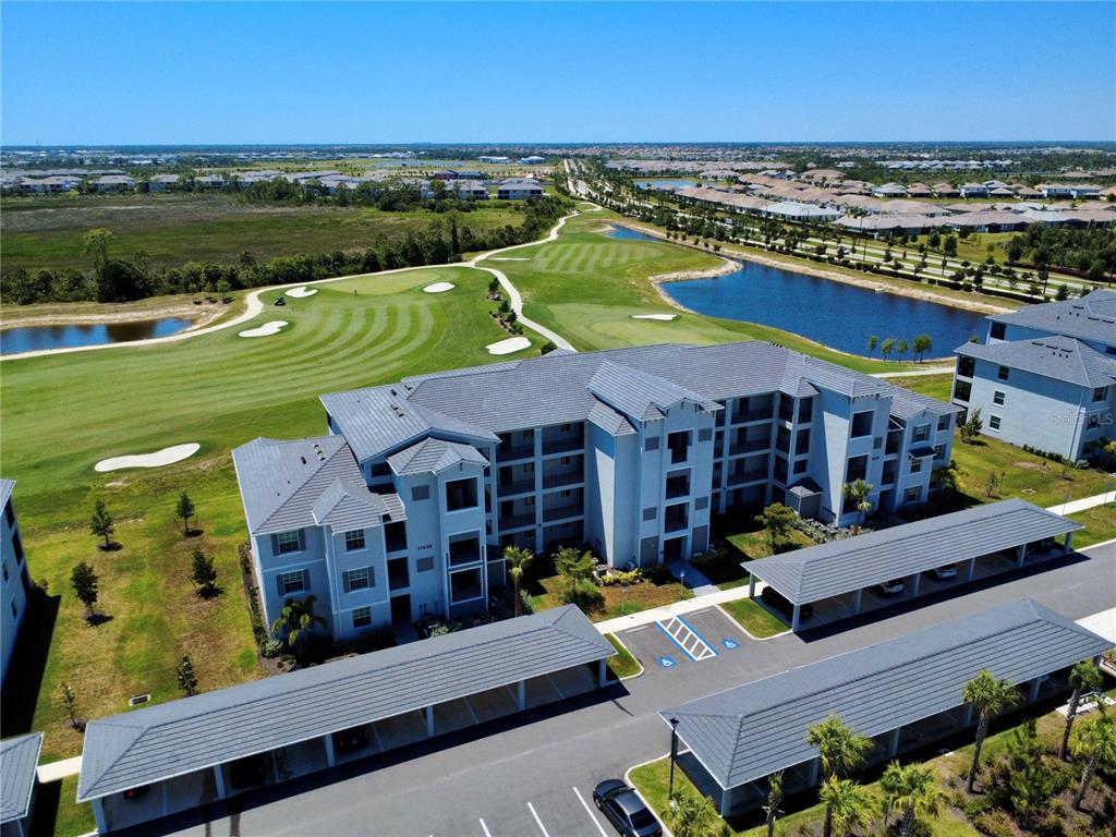 An aerial view shows a multi-story apartment building with covered parking next to a golf course — 17625 OPAL SAND DRIVE UNIT 304, VENICE, FL
