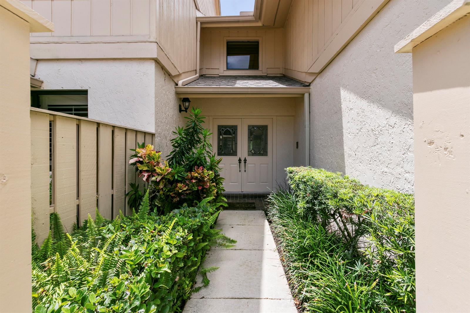 A concrete walkway leads to a double-door entrance framed by lush green landscaping — 17110 Waterbend Drive # 219, Jupiter FL 33477, JUPITER, FL