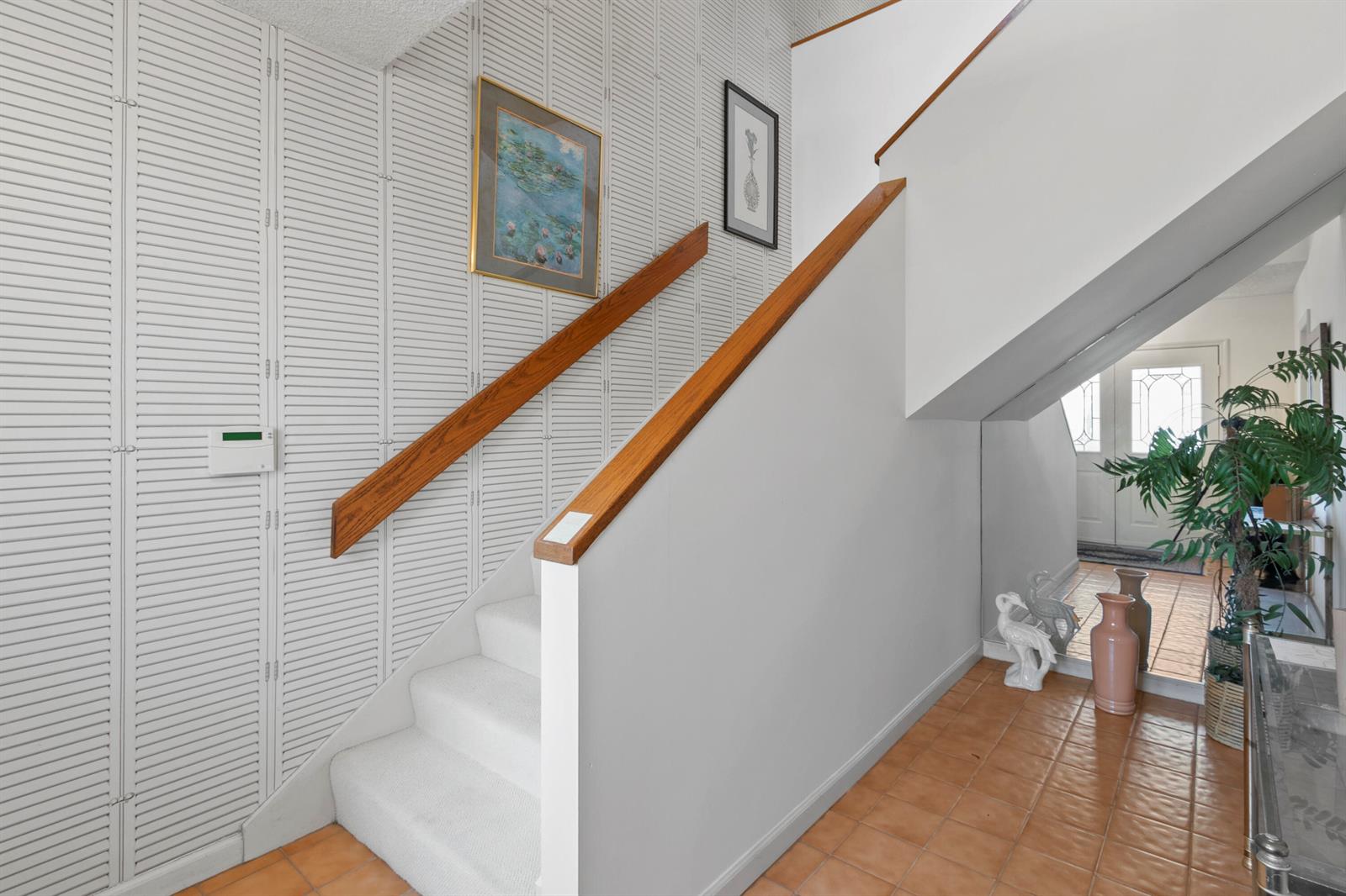 A staircase with white carpet and wooden handrails sits beside a wall covered in shutters — 17110 Waterbend Drive # 219, Jupiter FL 33477, JUPITER, FL
