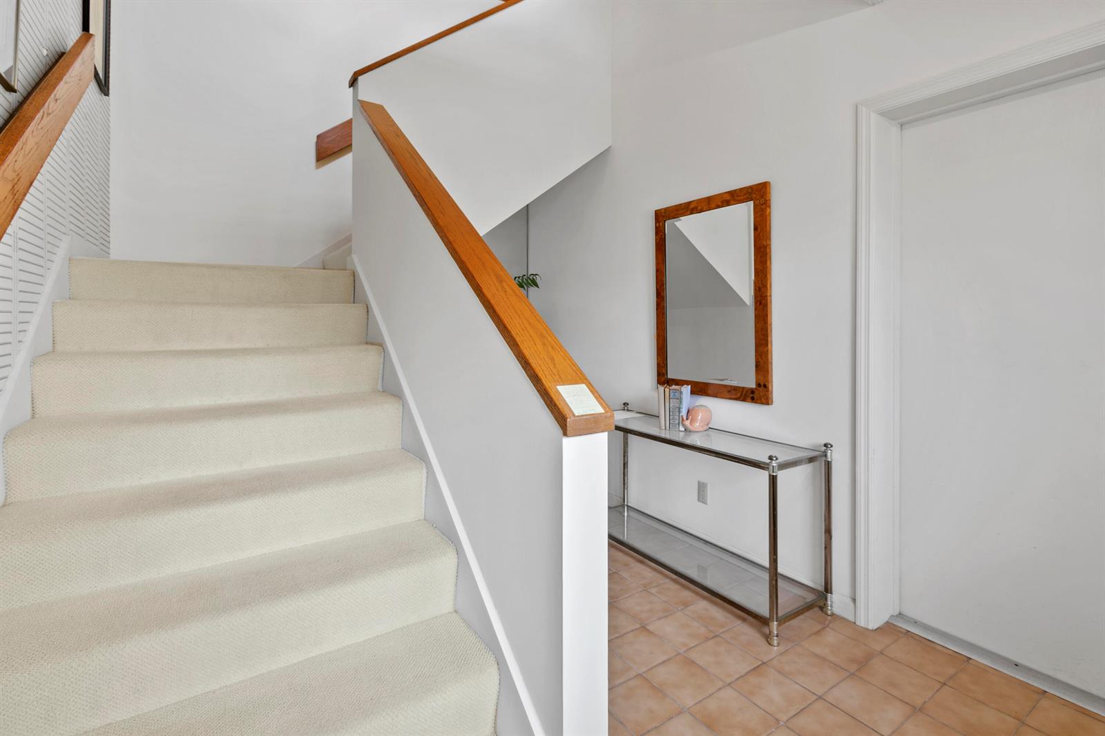 A carpeted staircase with a wooden handrail leads to a landing with a console table — 17110 Waterbend Drive # 219, Jupiter FL 33477, JUPITER, FL