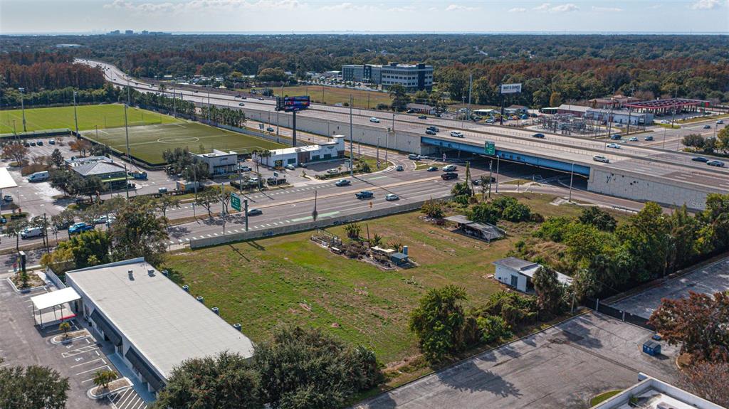 An aerial view shows a vacant lot adjacent to a commercial building and a highway overpass — 5711 W WATERS AVENUE, TAMPA, FL