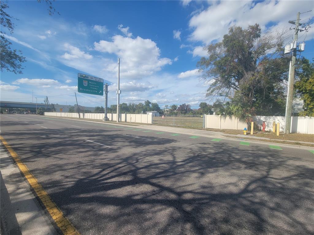 A paved road runs alongside a fenced, vacant lot with a highway sign overhead — 5711 W WATERS AVENUE, TAMPA, FL