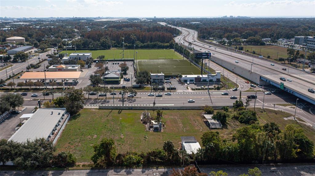 An aerial view shows a vacant lot in the foreground with commercial buildings and a highway — 5711 W WATERS AVENUE, TAMPA, FL