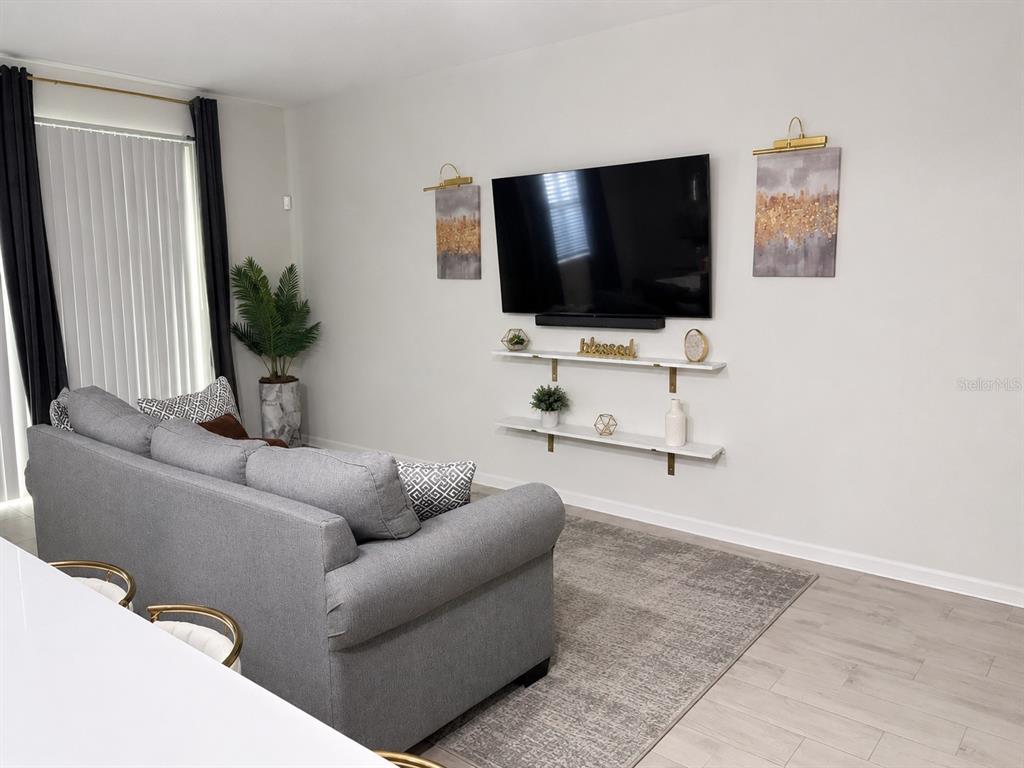 A living room features a grey sofa, a wall-mounted television, and two floating shelves — 10972 BRIGHTLEAF COURT, RIVERVIEW, FL