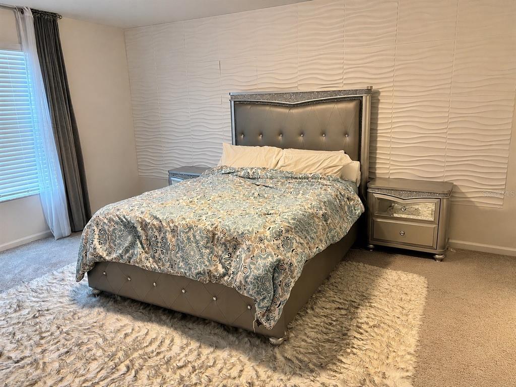 A bedroom features a tufted silver bed, matching nightstands, and a textured white accent wall — 10972 BRIGHTLEAF COURT, RIVERVIEW, FL